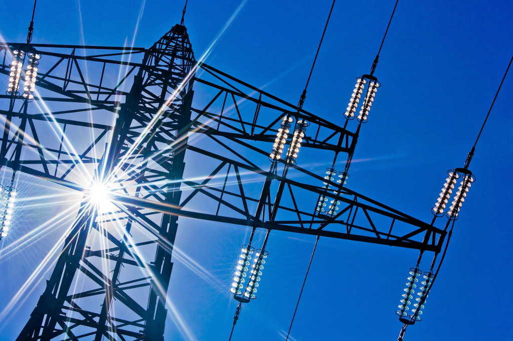 a high-voltage electricity pylons against blue sky and sun rays