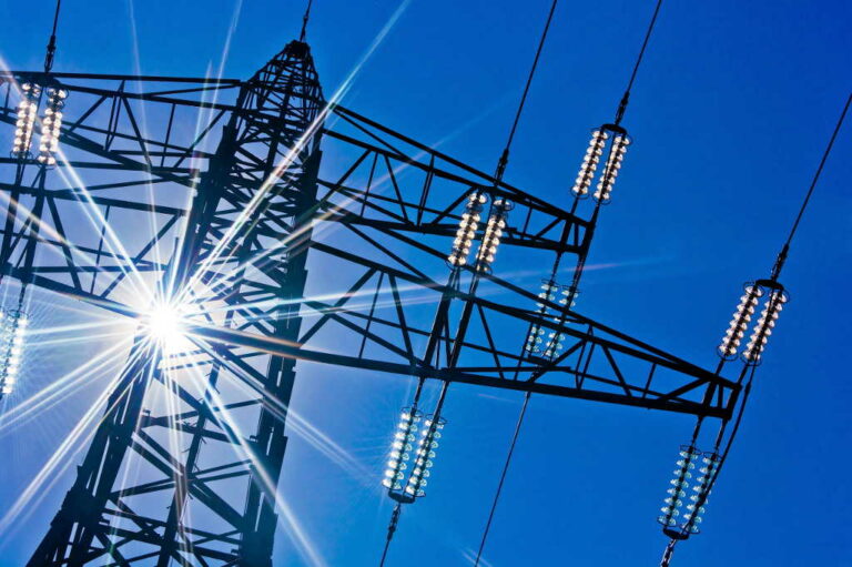 a high-voltage electricity pylons against blue sky and sun rays