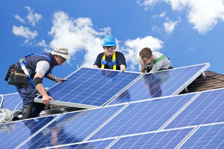 Workers installing alternative energy photovoltaic solar panels on roof