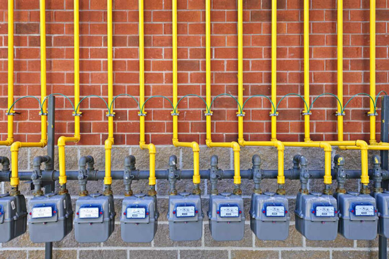 Row of natural gas meters with yellow pipes on building brick wall