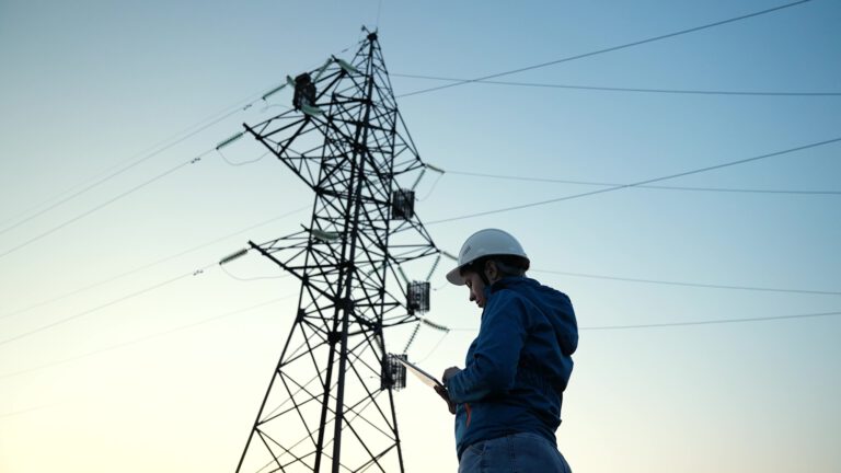 Power engineer woman engineer in protective helmet works outdoors High voltage electrical lines at sunset. Distribution, supply of electricity. Environmentally friendly electrical energy. Electrician