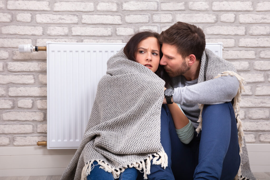 Couple In Blanket Sitting In Front Of Radiator Against Wall