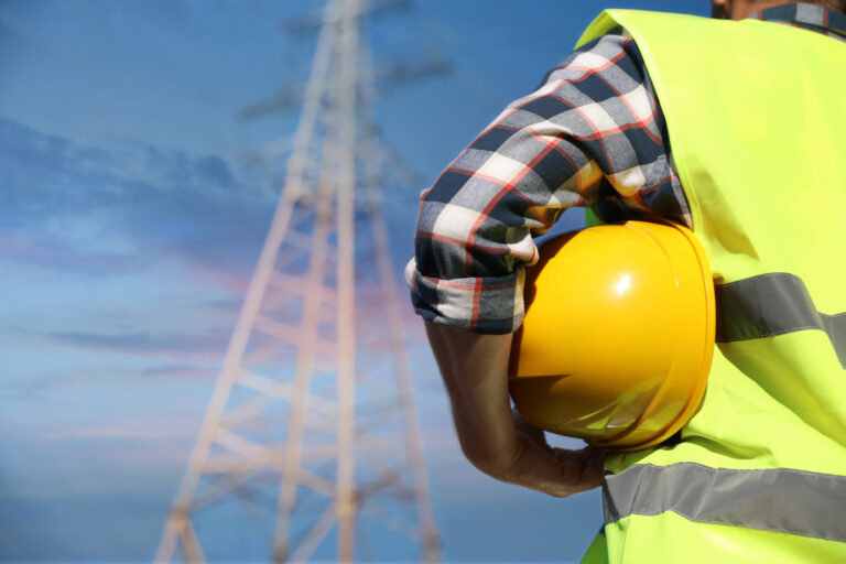 Professional electrician with helmet near high voltage tower, cl