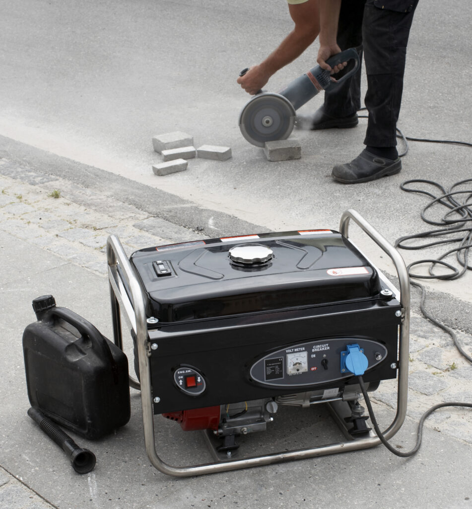 Electrical generator in foreground and man using masonry saw